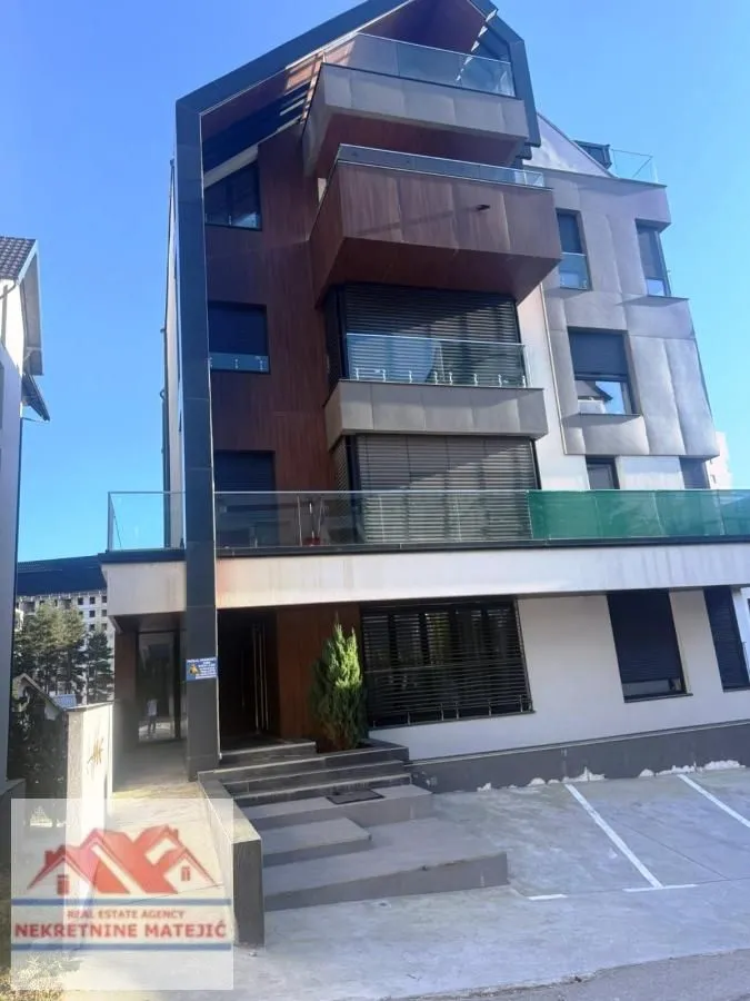 Pogled na spoljašnjost moderne stambene zgrade sa terasama i parkingom.
