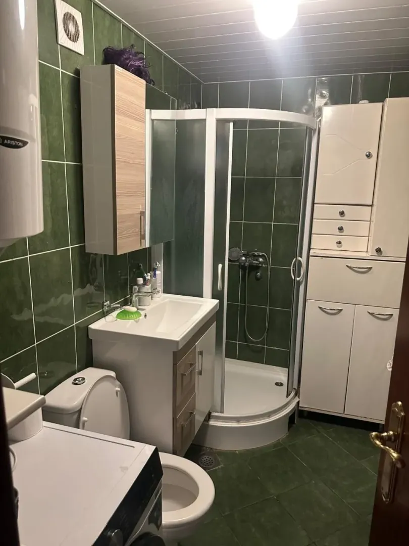Kupatilo sa tuš kabinom, umivaonikom i zelenim pločicama na zidovima.