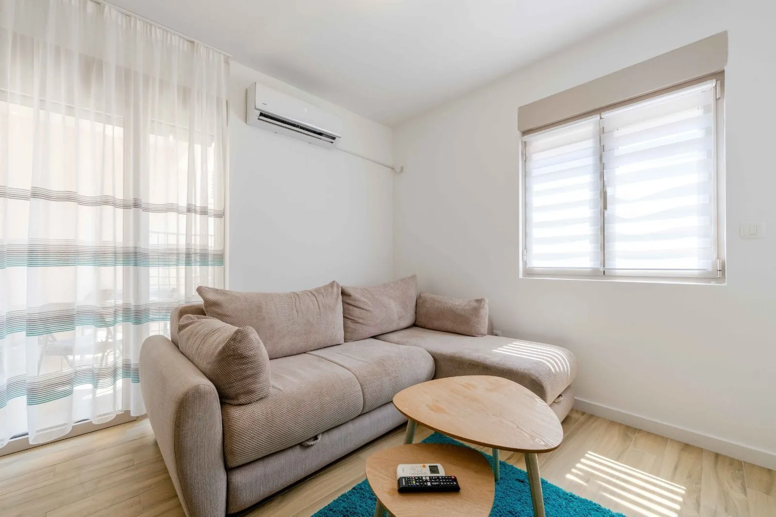 Corner sofa in a bright living room with an air conditioner and windows.