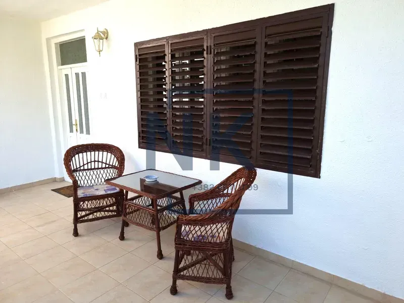Covered terrace with wicker seating furniture in front of a white facade.