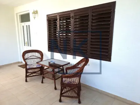 Covered terrace with wicker seating furniture in front of a white facade. - image 12