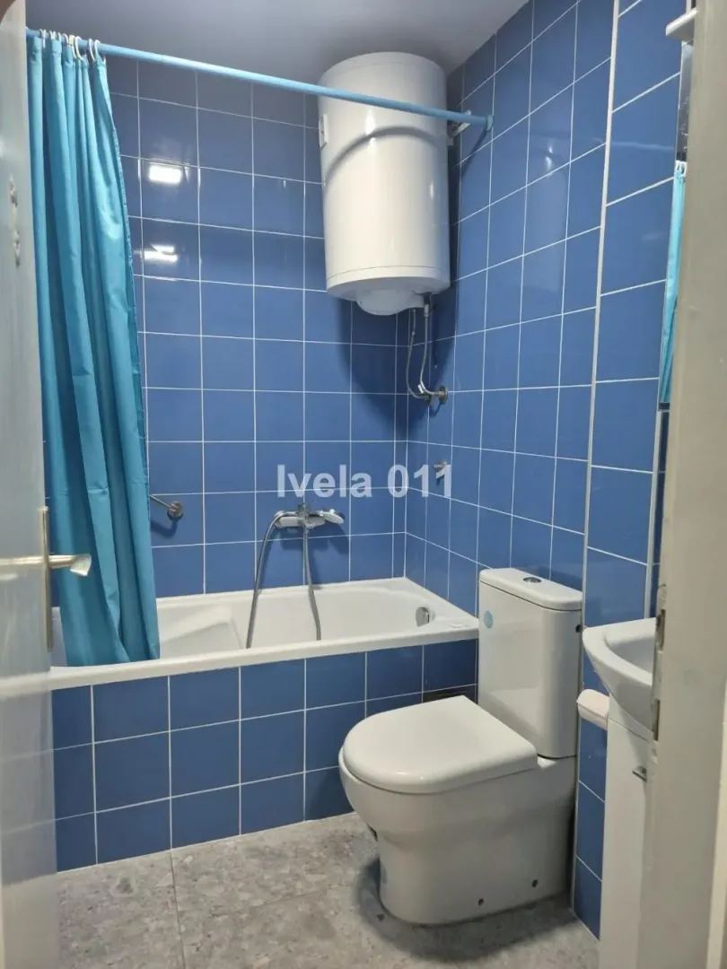 Small bathroom with blue tiles, bathtub, toilet, and water heater.