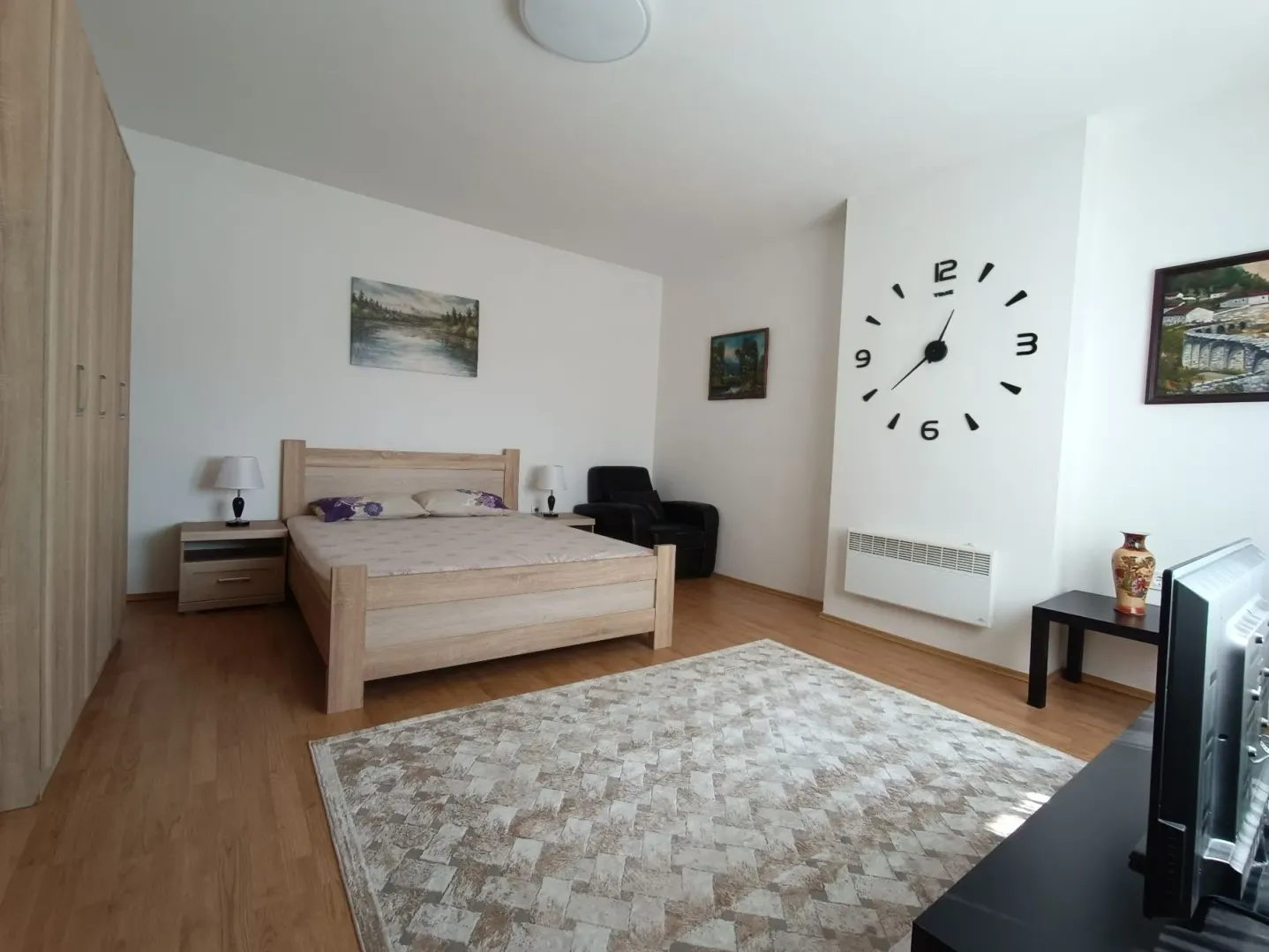 Spacious bedroom with a double bed, wardrobe, and a large wall clock.