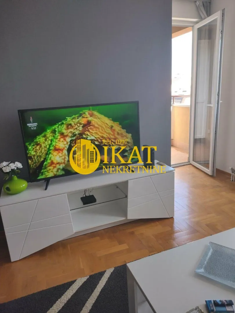 Dnevna soba sa TV komodom i izlazom na terasu.