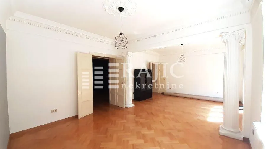Empty living room with parquet flooring and decorative columns.