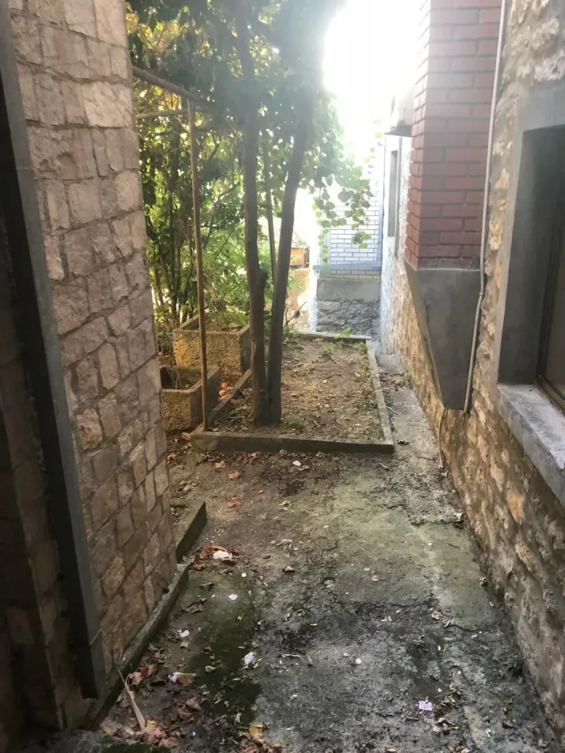 Prolaz između kamenih zidova sa manjim dvorišnim prostorom i drvećem.