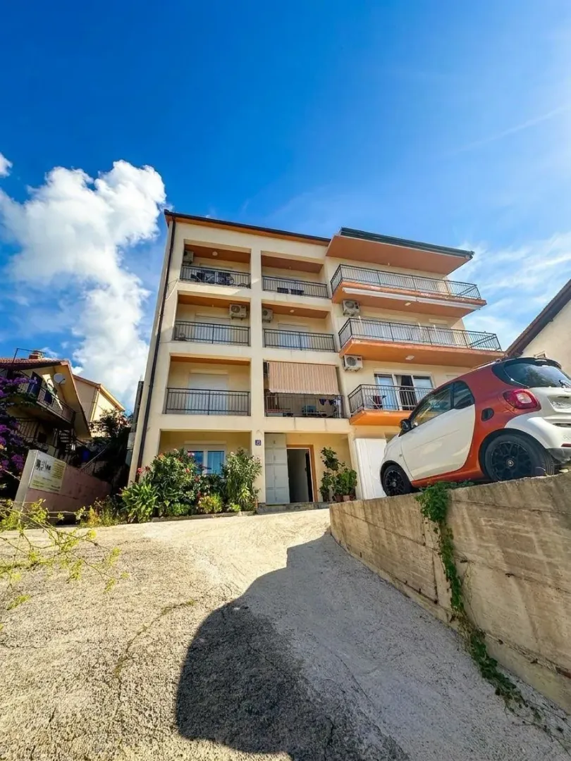 Pogled na spoljašnjost stambene zgrade sa prilazom i parkiranim automobilom.