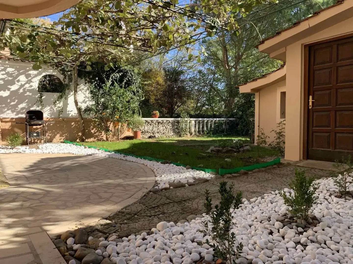 Landscaped yard with paved pathways, decorative stones, and a barbecue grill.
