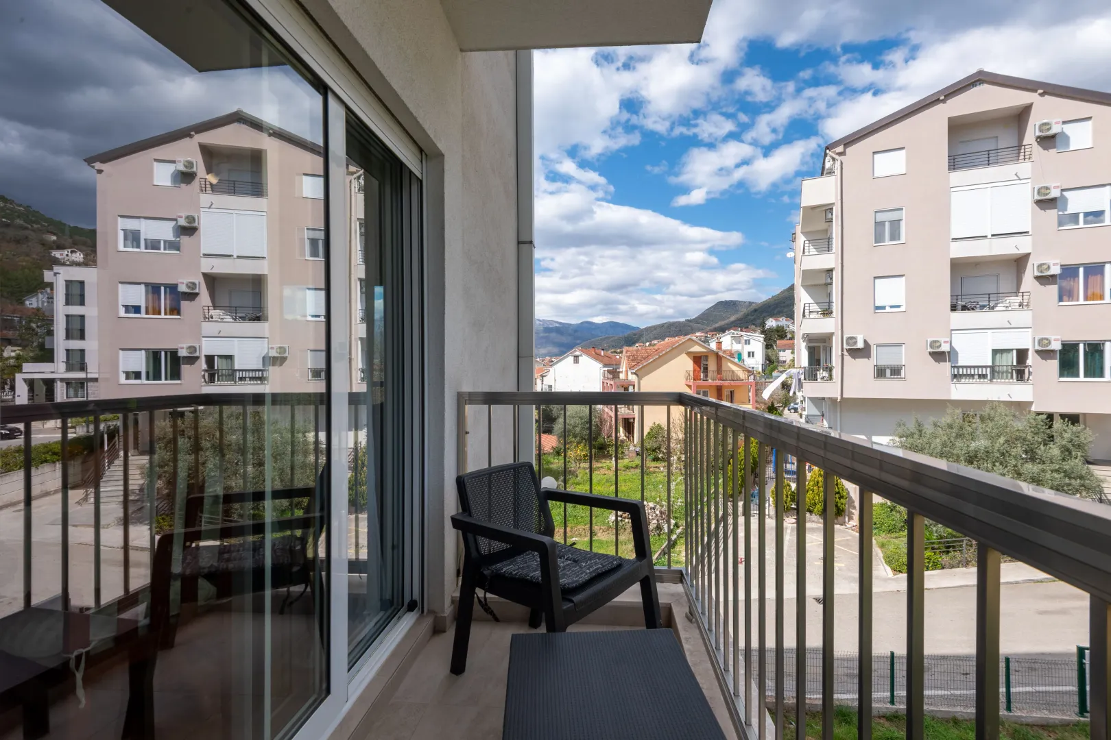 Namješten balkon sa stolicom i pogledom na okolne zgrade i brda.