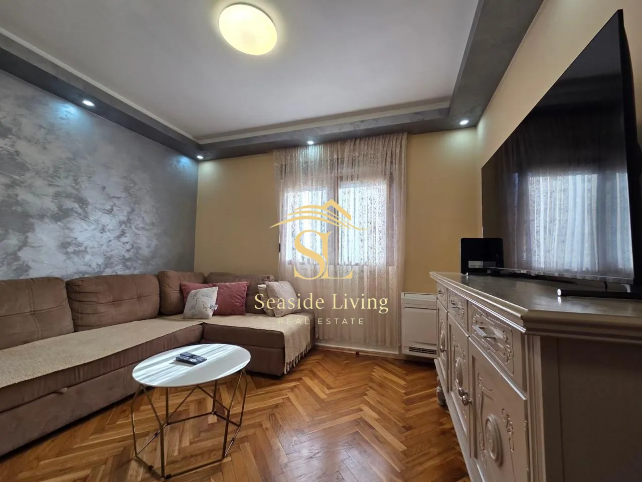 Living room with a sectional sofa, TV, and parquet flooring.