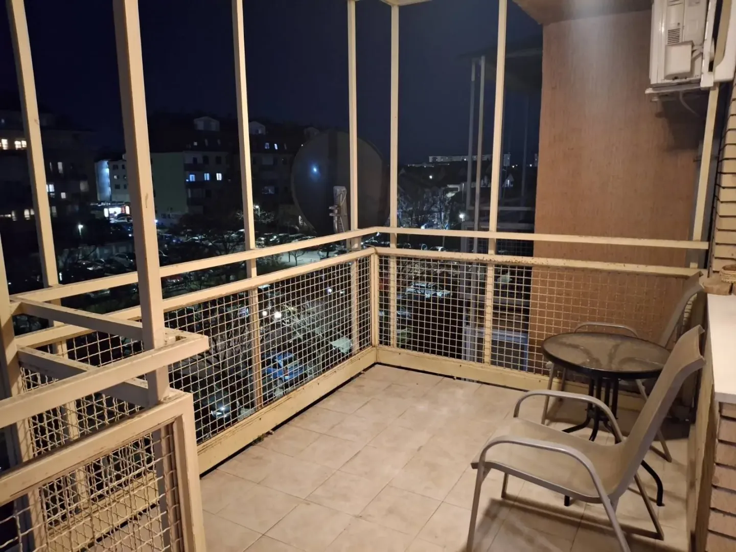 Prostrani balkon sa garniturom za sjedjenje i pogledom na grad noću.