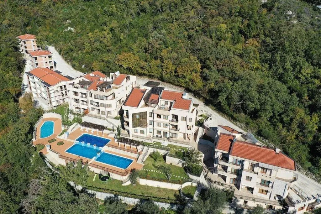 Pogled iz vazduha na stambeni kompleks sa bazenima okružen zelenilom.