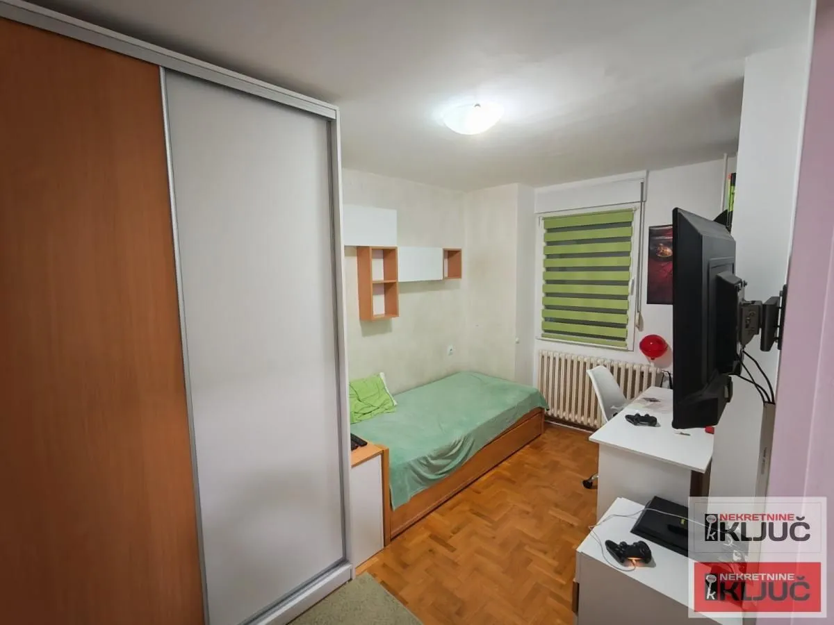 Dečja soba sa krevetom, radnim stolom i velikim ormarom.