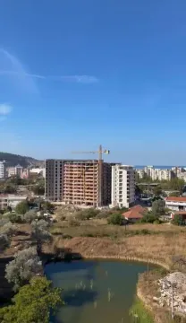 View of a building under construction and the surrounding landscape with a small water basin in the foreground. - image 9