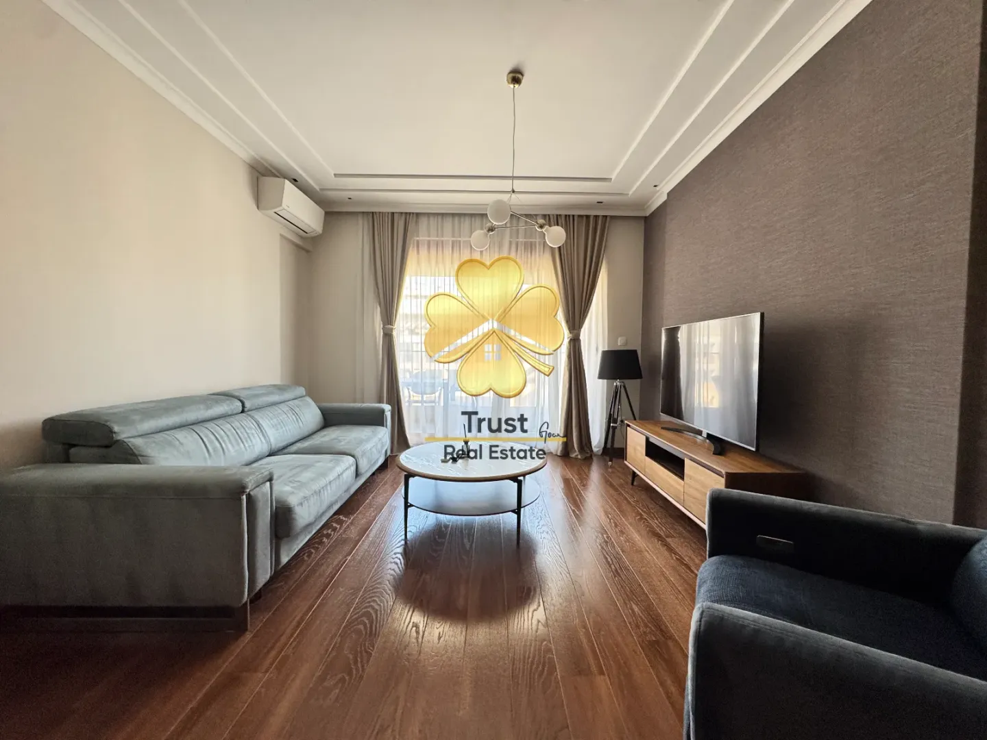 Spacious living room with a sofa, TV unit, and wooden flooring.