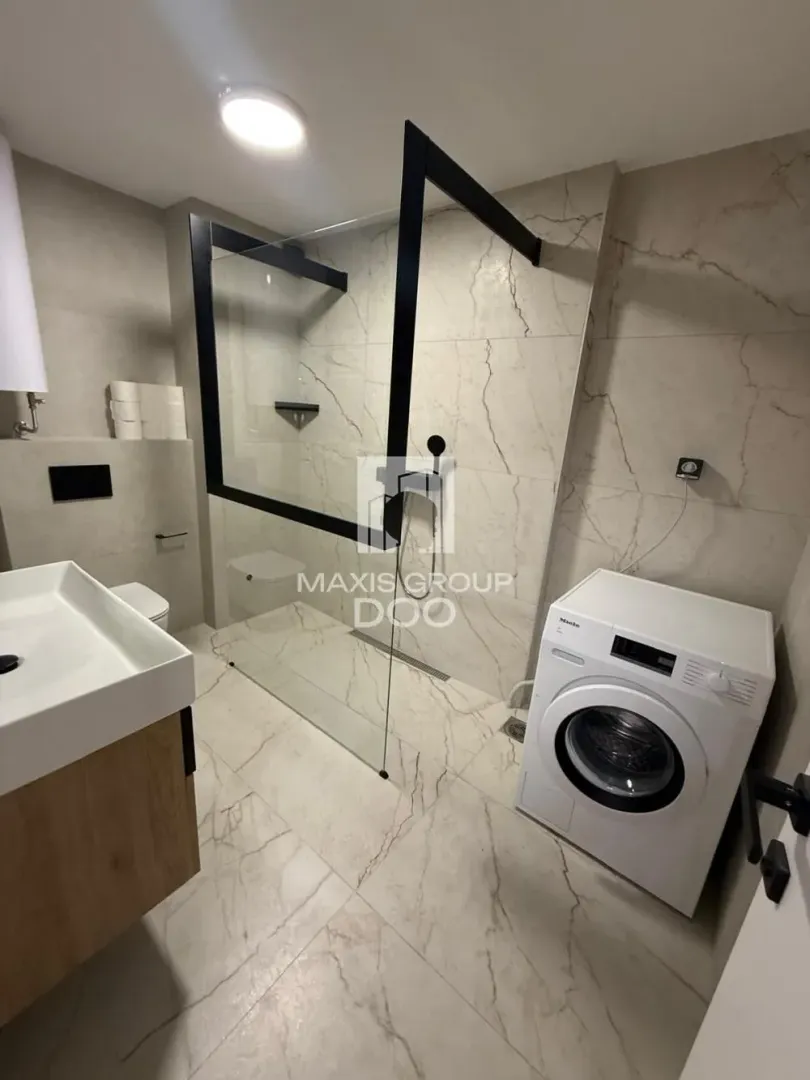 Modern bathroom with a walk-in shower, washbasin, and washing machine.