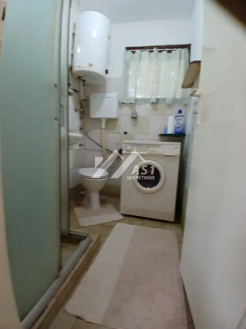 Manje kupatilo sa tuš kabinom, WC šoljom i veš mašinom.
