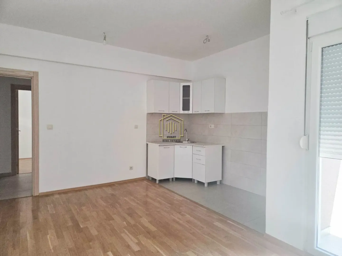 Manja bijela kuhinja u uglu prostorije sa drvenim podom.
