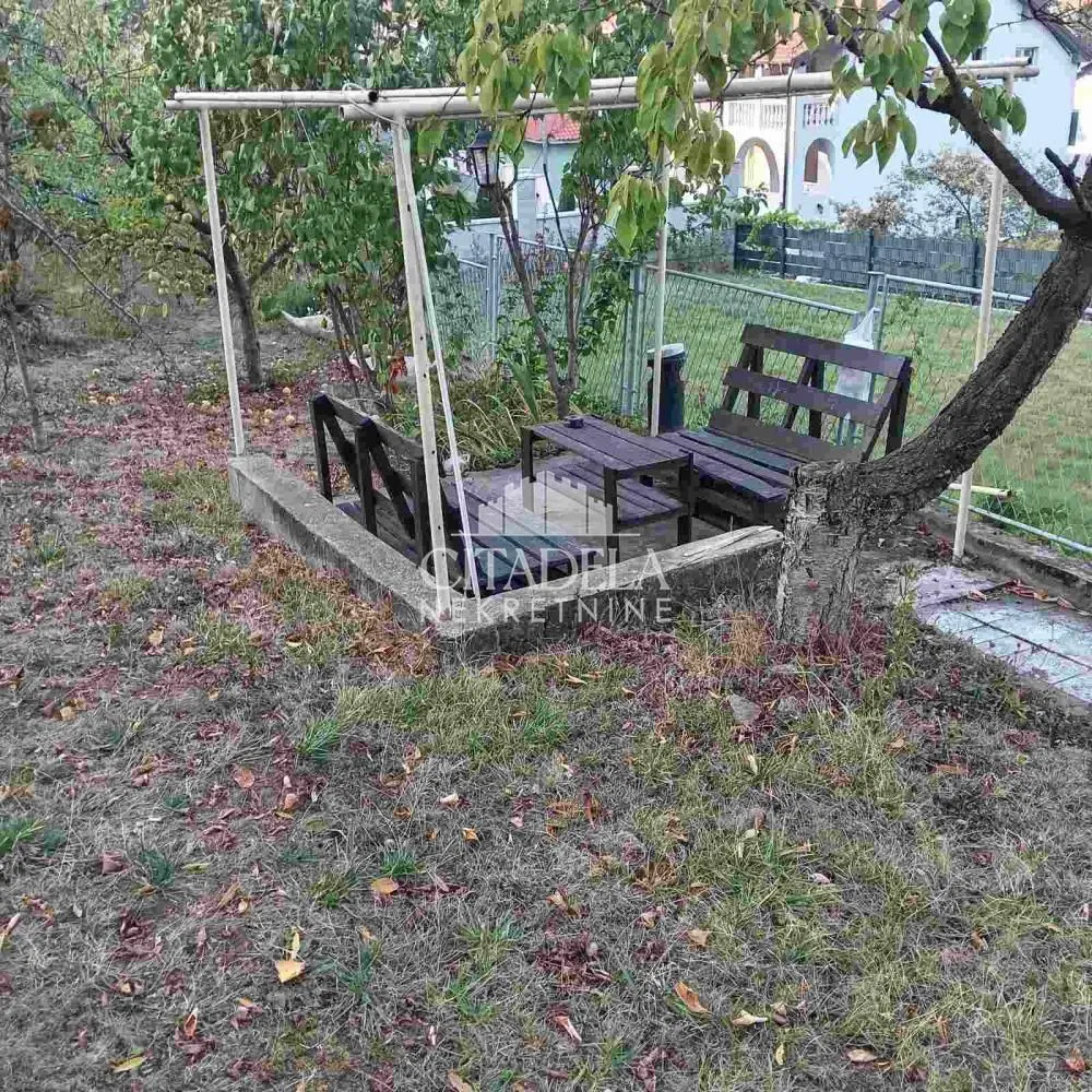 Dvorište sa drvenom klupom i stolom ispod nadstrešnice.