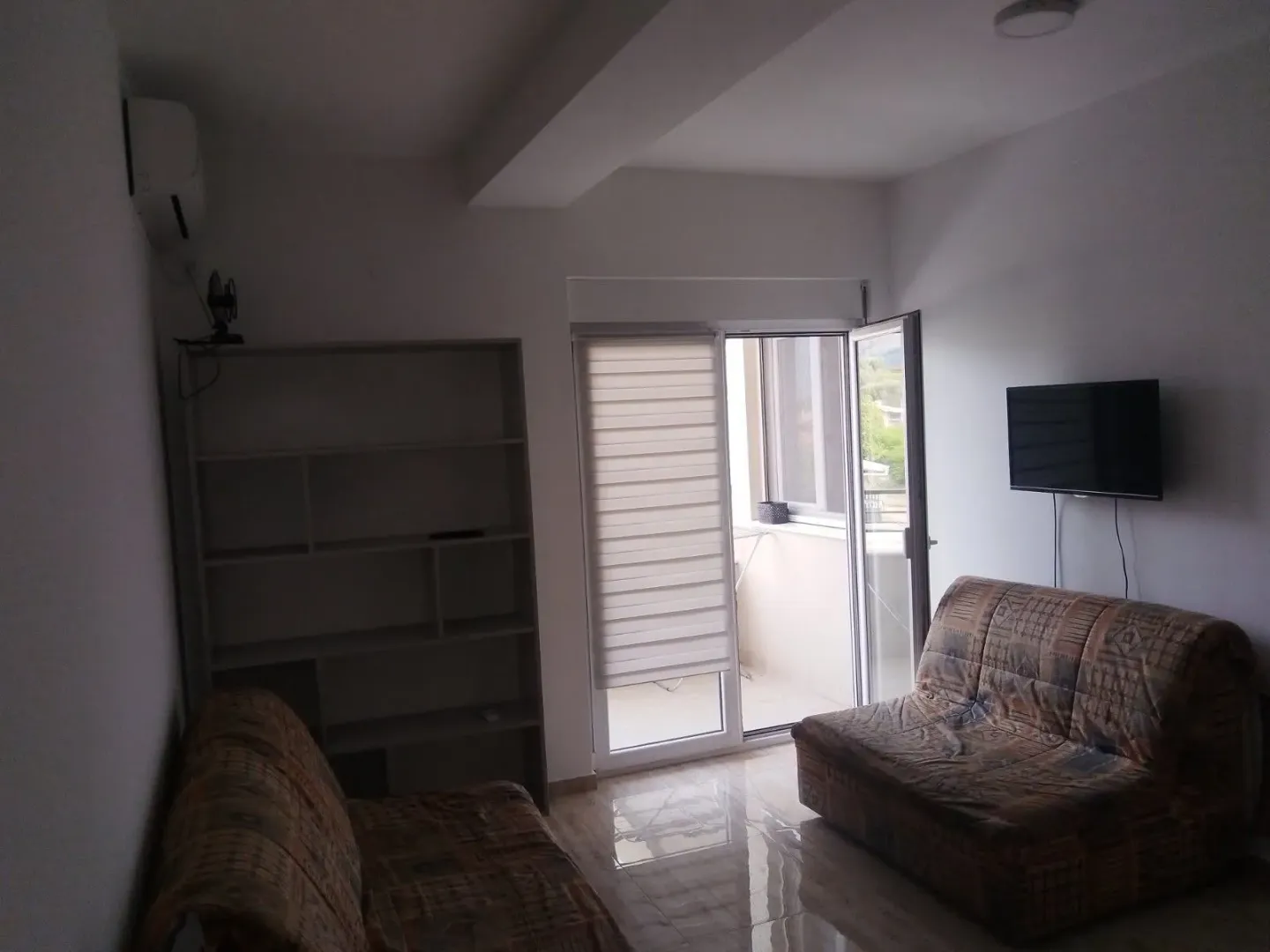 Living room with sofa, shelving unit and access to the balcony.