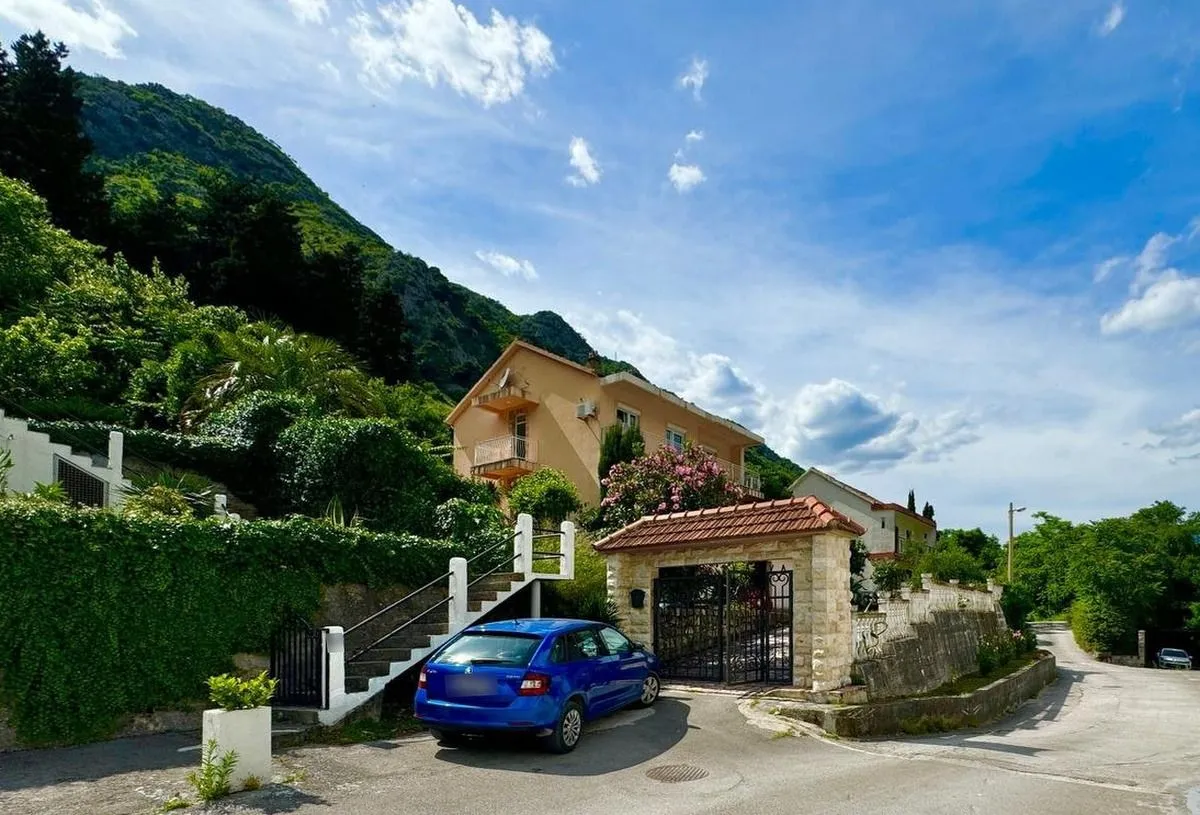 Pogled na spoljašnjost kuće sa dvorištem, kapijom i parkiranim automobilom.