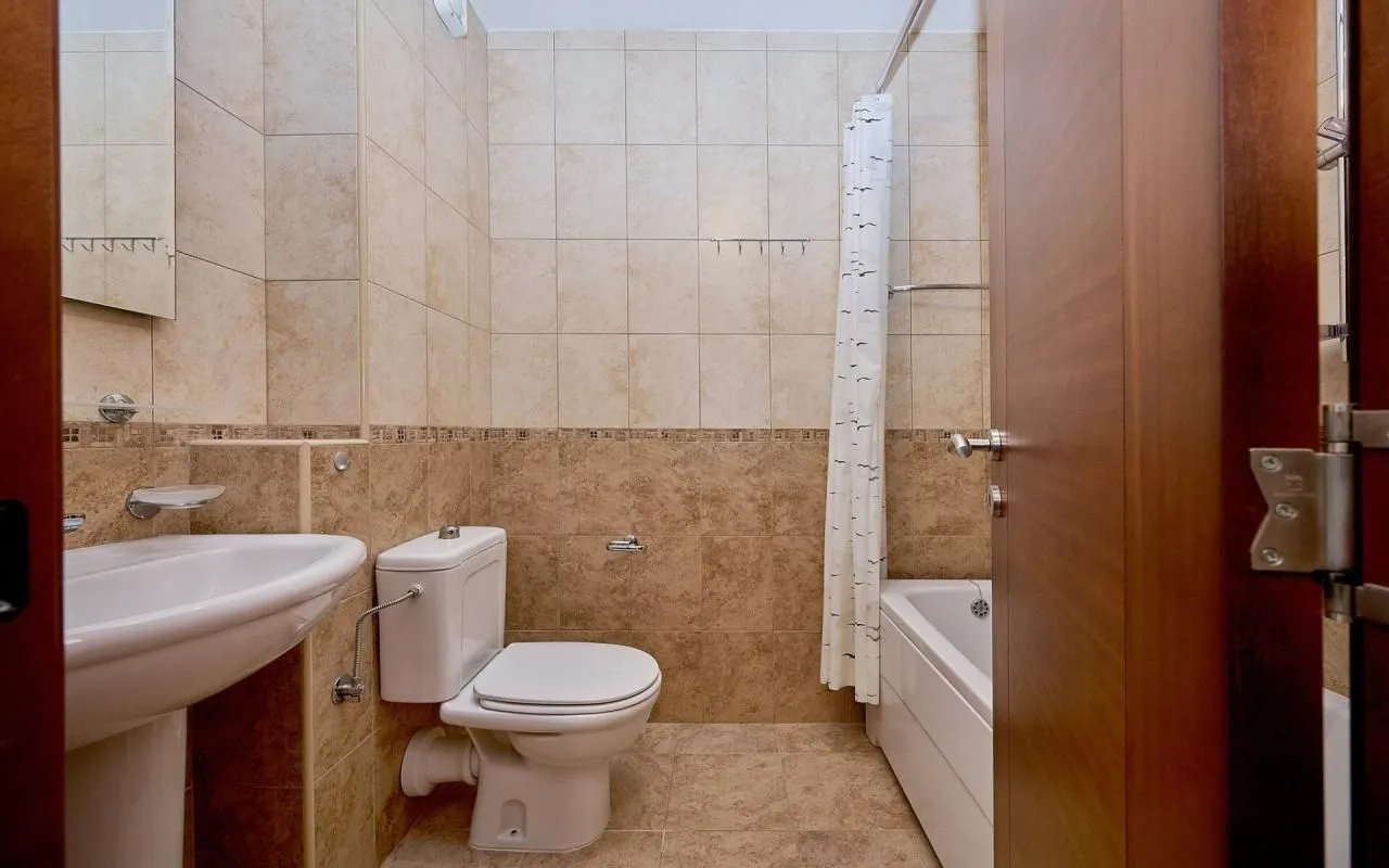 Small tiled bathroom with a washbasin, toilet bowl, and bathtub.