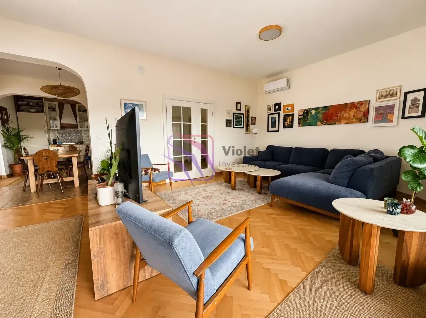 Living room with a sofa, armchairs and a television, overlooking the dining area.