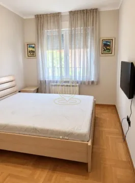 Spavaća soba sa bračnim krevetom, prozorom sa zavesama i zidnim televizorom. - image 4