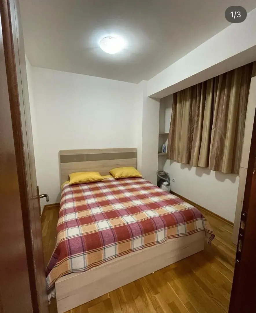 Bedroom with a double bed, wooden flooring, and a window with curtains.