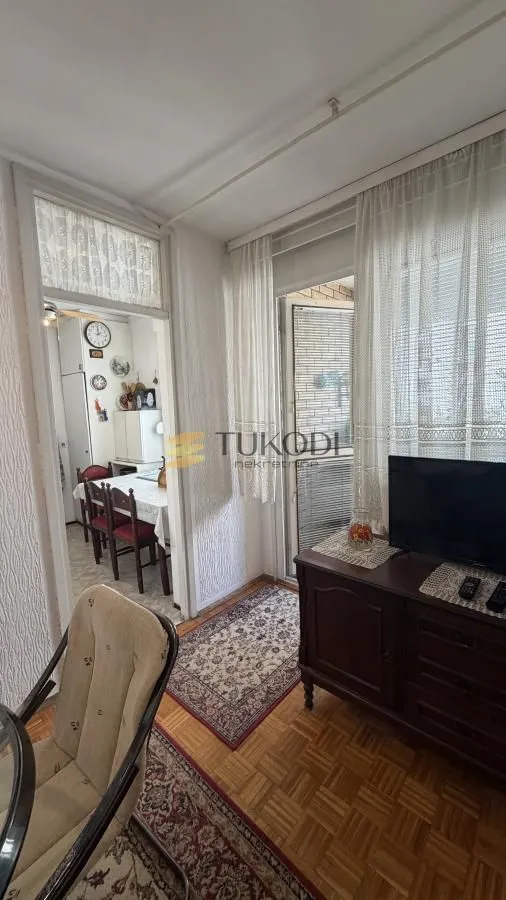 Dnevna soba sa TV komodom i izlazom na terasu, sa pogledom na trpezariju.