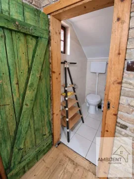 Pogled kroz drvena vrata na manje kupatilo sa wc šoljom i policama. - image 17