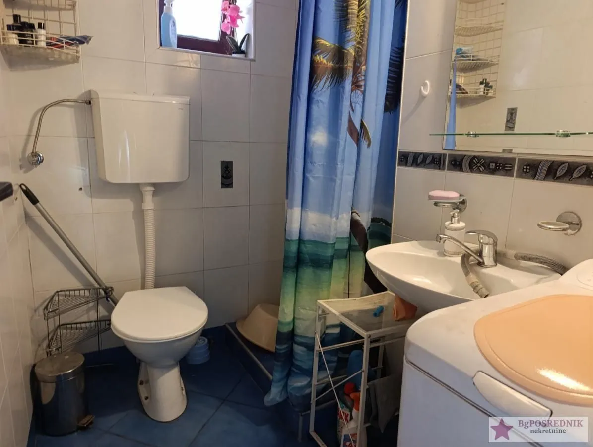 Manje kupatilo sa toaletom, umivaonikom i tuš kabinom sa zavesom.