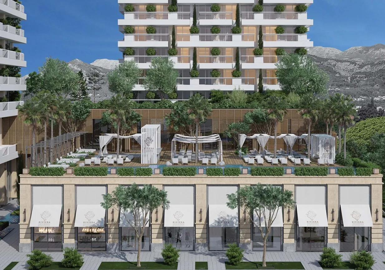 Pogled na spoljašnjost moderne stambene zgrade sa uređenom terasom i lokalima u prizemlju.