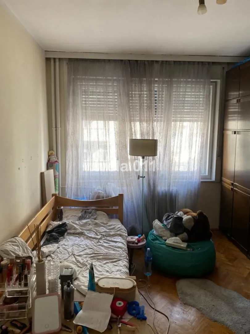 Manja spavaća soba sa krevetom, garderoberom i prozorom sa zavesama.