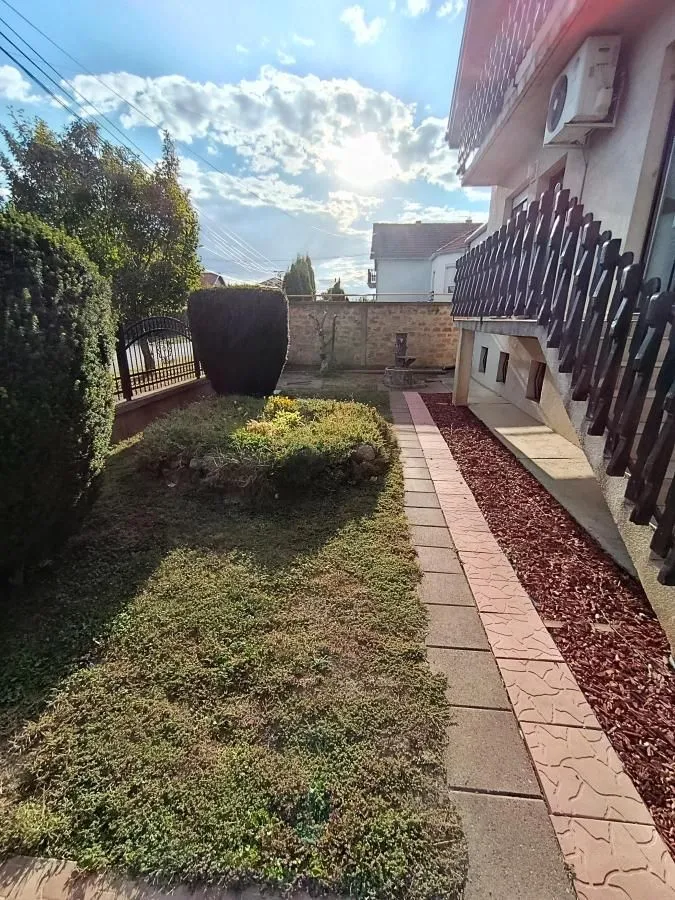 Pogled na uređeno dvorište kuće sa stazom i zelenilom.