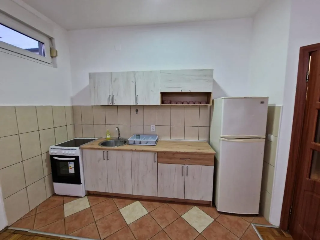 Manja kuhinja sa bijelim elementima, šporetom i frižiderom.