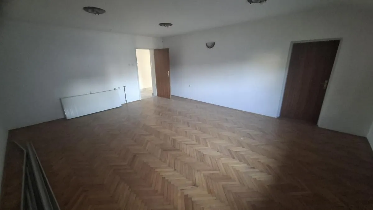Prazna soba sa parketom i belim zidovima.