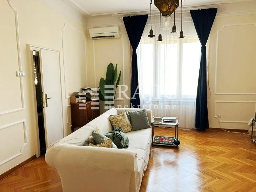 Spacious and bright living room with a sofa and parquet flooring.
