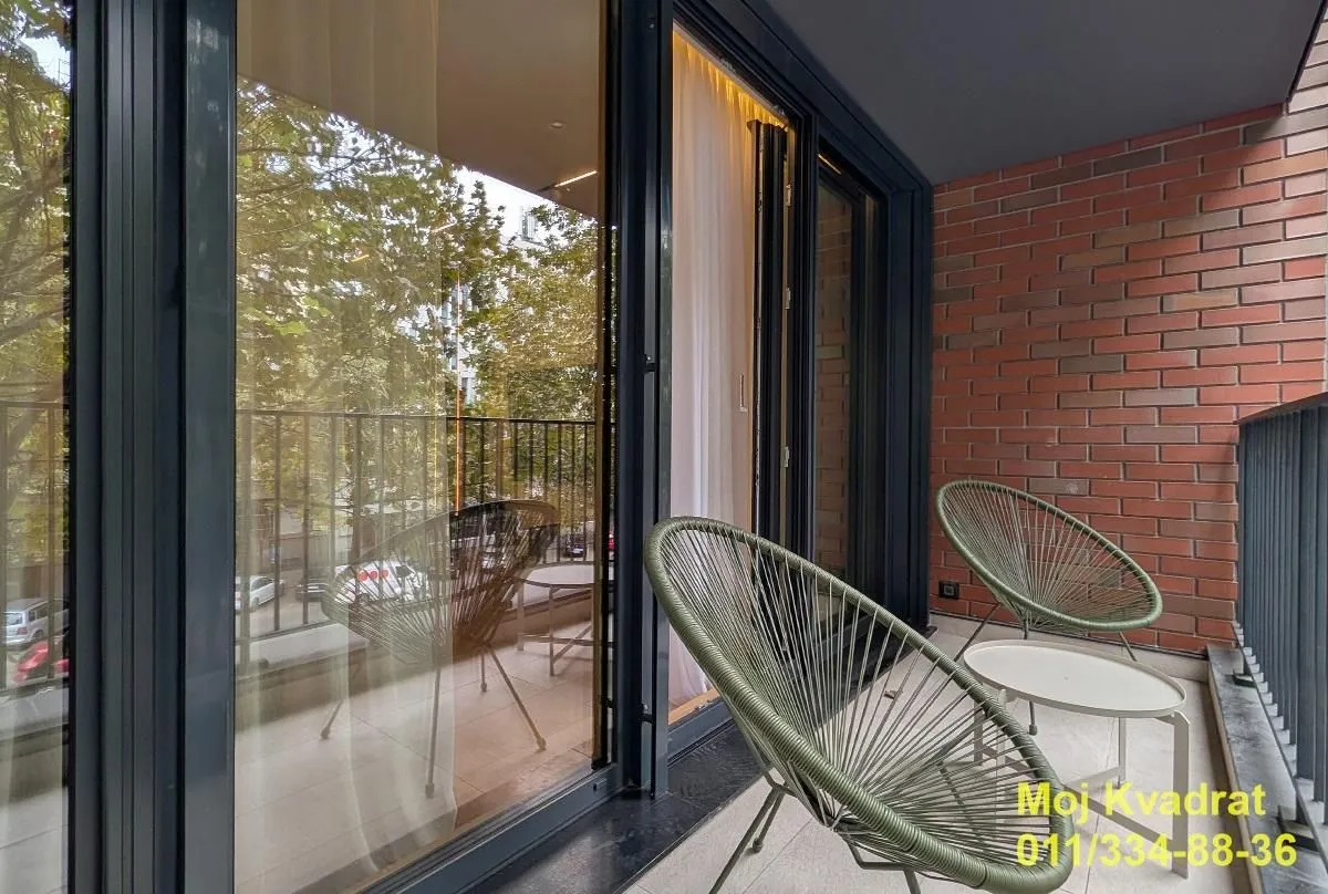 Furnished balcony with glass railing and green view.