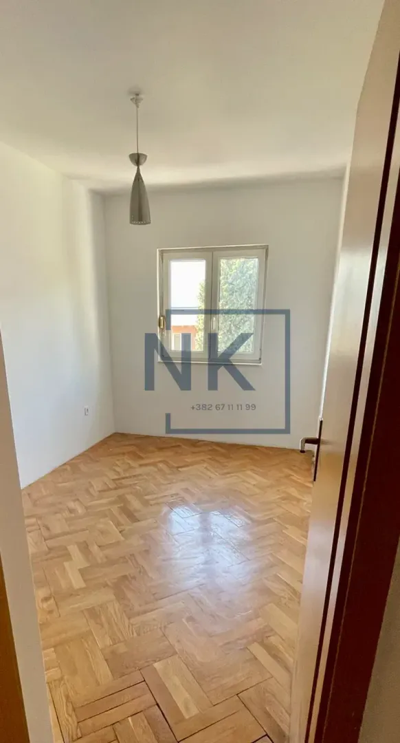 An empty room with parquet flooring and a single window.