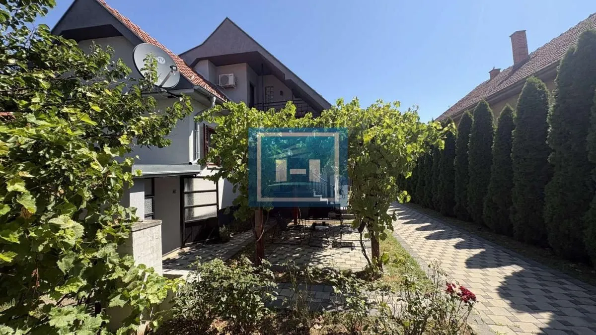 Pogled na dvorište i spoljašnjost kuće sa uređenom stazom i zelenilom.