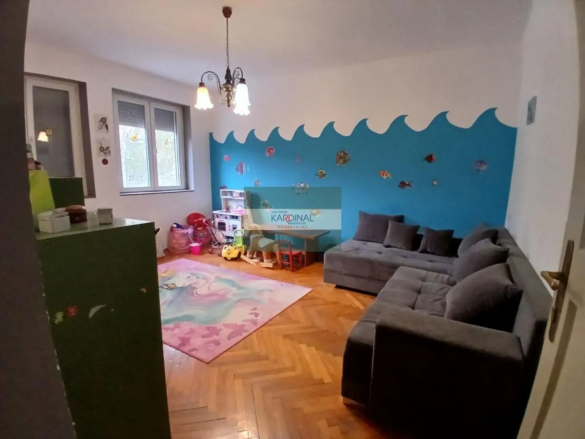 Dnevna soba sa ugaonom garniturom, parketom na podu i dečijim kutkom.