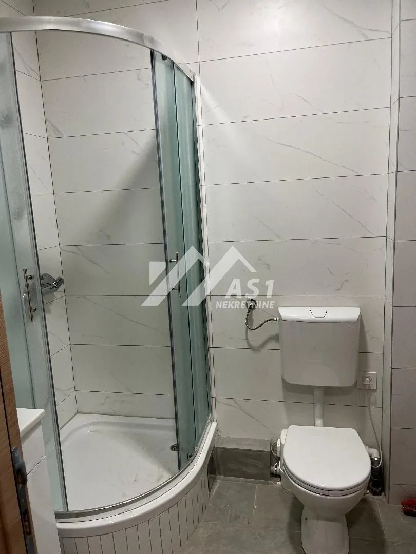 Manje kupatilo sa tuš kabinom i belim keramičkim pločicama.