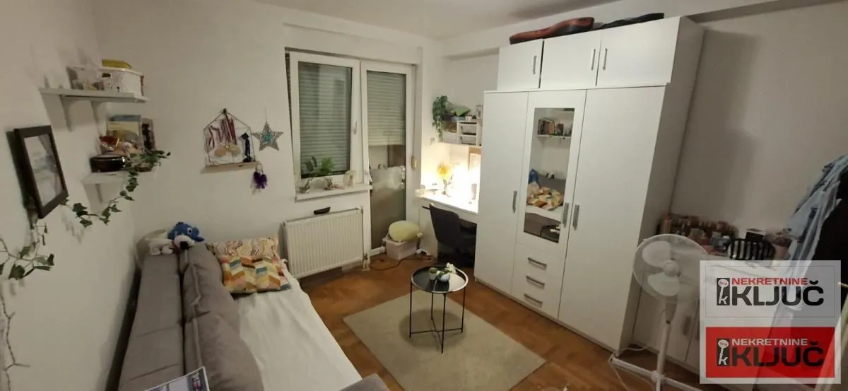 Manja spavaća soba sa krevetom, belim garderoberom i radnim stolom.