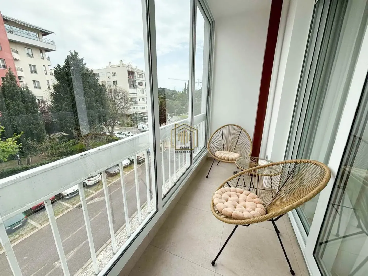 Zastakljeni balkon sa garniturom za sjedenje i pogledom na grad.