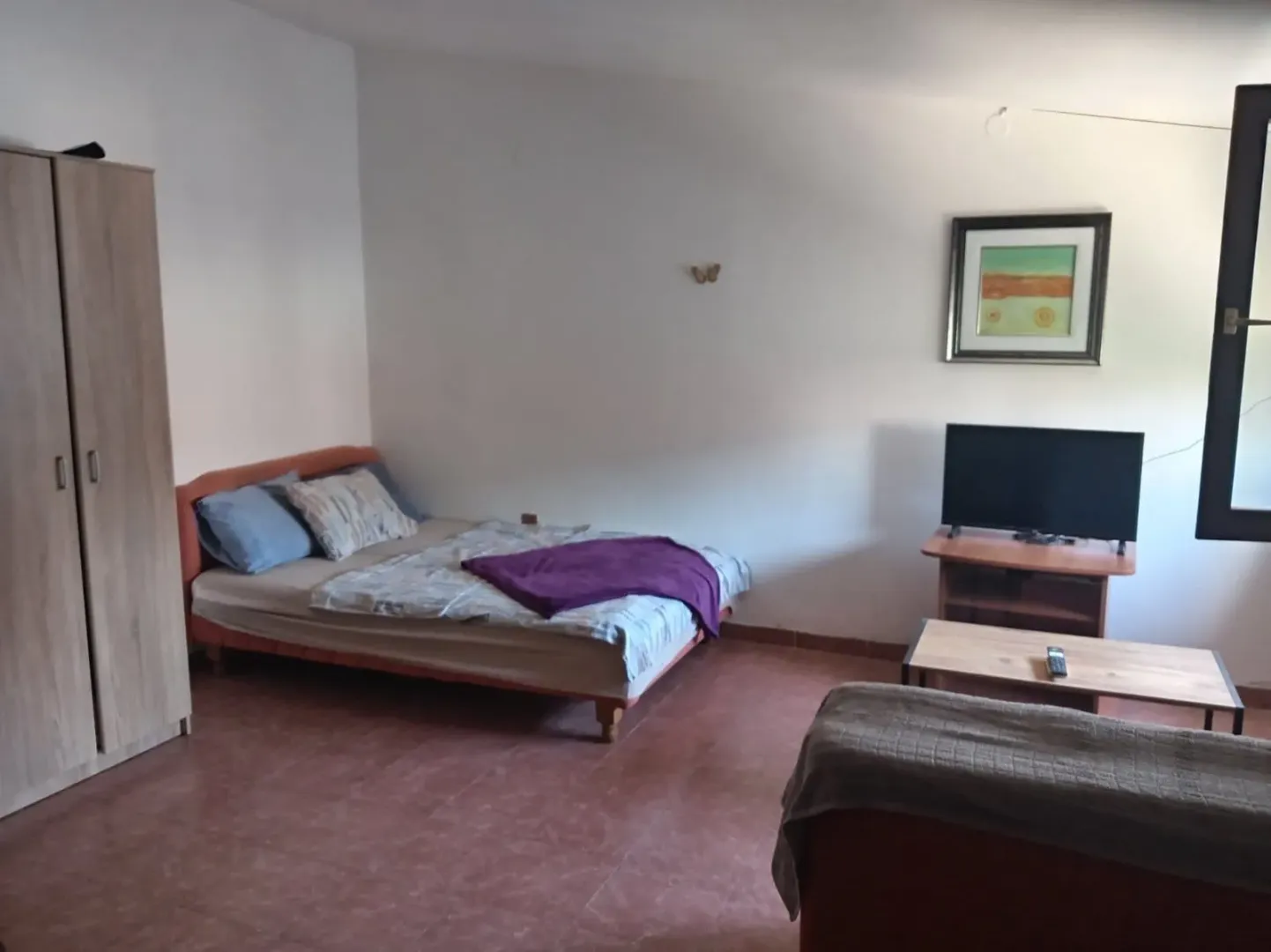 Furnished bedroom with a bed, wardrobe, and television.