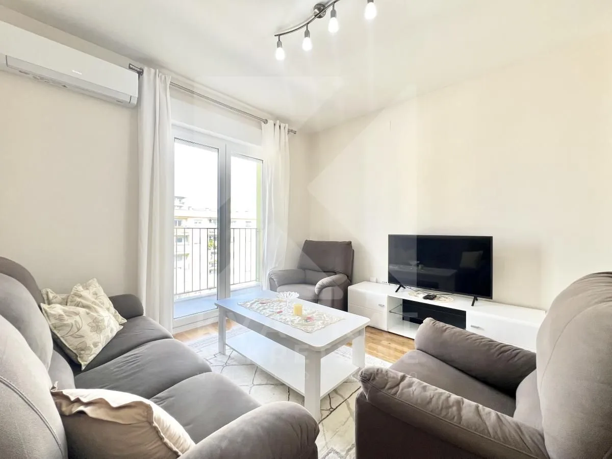 Living room furnished with a sofa set, television, and access to a balcony.