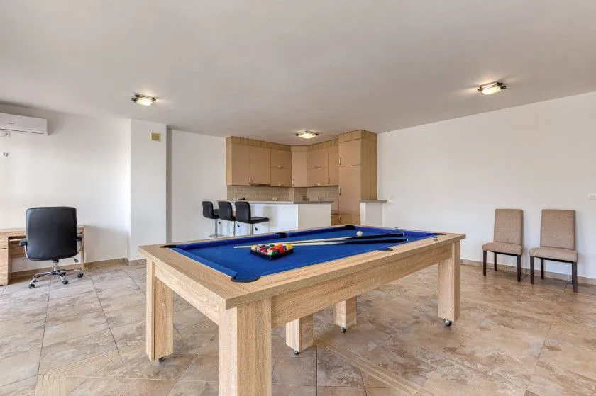 Living room with a pool table and a kitchen in the background.
