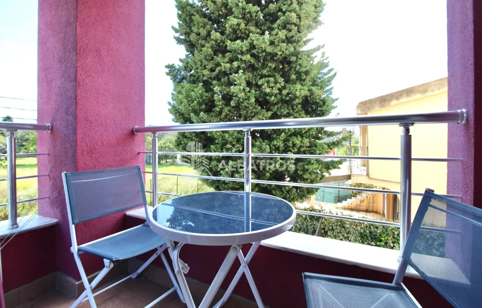 Covered balcony with a table and two chairs and a view of greenery.