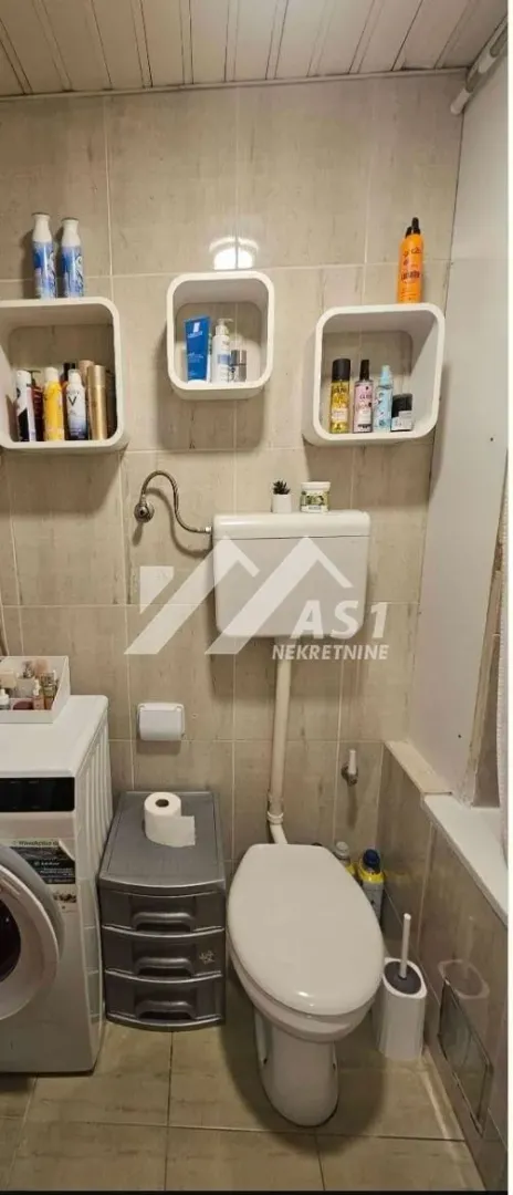 Smaller bathroom with a toilet, washing machine, and wall shelves.